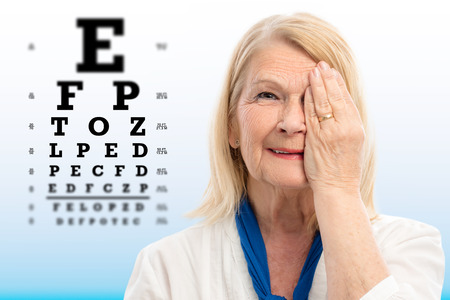 Close up portrait of senior woman testing vision Woman closing one eye with hand.Alphabet test chart with focus point in background.の写真素材