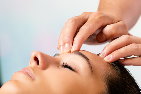 Close up portrait of woman enjoying beauty treatment. Therapist hands massaging forehead.の写真素材