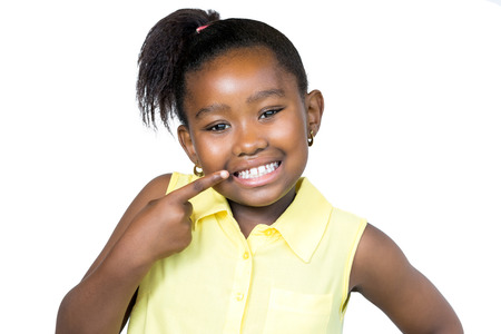 Close up  portrait of cute little african girl with ponytail pointing with finger at teeth.Isolated on white background.の写真素材