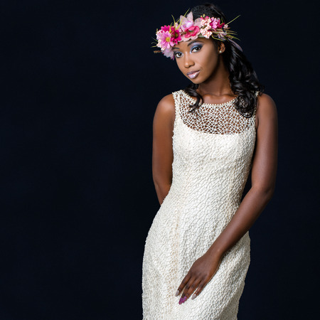 Close up studio portrait of attractive young african bride wearing white wedding gown. Medium shot of girl with colorful flower garland against dark background.の写真素材