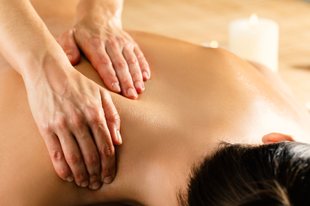 Close up macro detail of hands massaging female upper back and shoulder in spa. Ambient candlelight in background.の写真素材