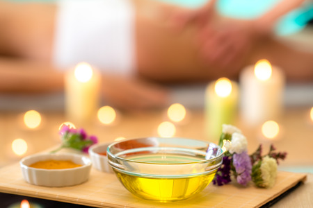 Macro close up still life of glass bowl with Ayurvedic massage oil. Out of focus background with therapist massaging woman.の写真素材