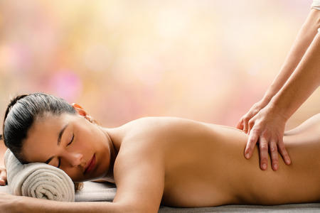 Medium side view portrait of young woman having hot aromatic oil massage is spa.Therapist applying pressure on spinal column.の写真素材