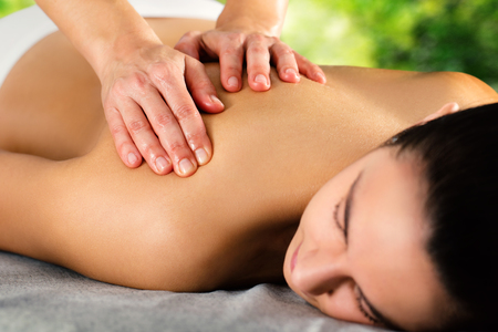 Close up of hands massaging female back and shoulder against green background.の写真素材