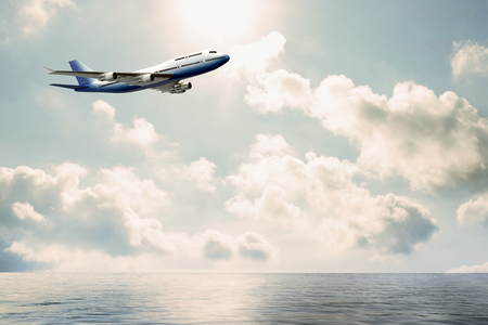 Side view of commercial jumbo  flying over water. Blue and white airplane with copy space against cloud background.の写真素材