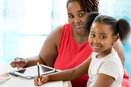 Close up portrait of little african girl doing school work. Mother helping and supervising kid at home.の写真素材
