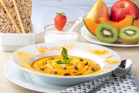 Close up of healthy diet menu. Appetising pumpkin soup with fresh fruit, organic kefir and crispy sesame seed crackers and bread sticks.の写真素材