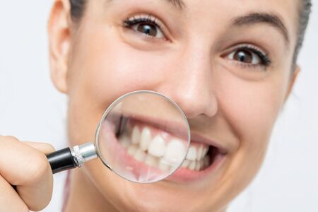 Close up fun portrait of young girl showing teeth with magnifying glass. Isolated on white background.の写真素材