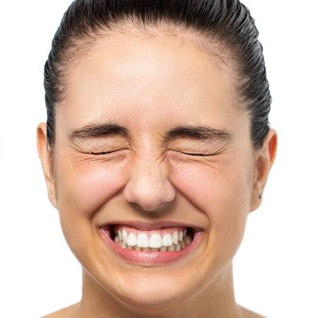 Close up face shot of young woman with eyes closed tensing eyes. Happy laughing girl isolated on white background.の写真素材