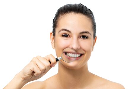 Close up portrait of young girl holding magnifying glass in front of healthy teeth. Isolated on white background.の写真素材