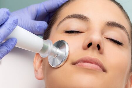 Macro close up of woman having facial mesotherapy. Therapist applying flat head plasma pen on cheek.