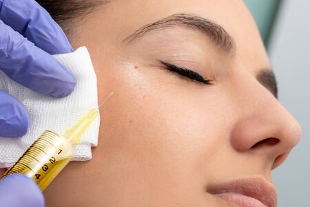 Macro close up of syringe with needle next to woman's face. Therapist doing cosmetic hormone treatment on girl.の写真素材