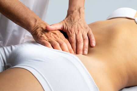 Close up of physiotherapist stimulating female colon intestine. Hands massaging abdomen.の写真素材