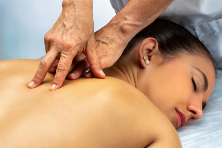 Close up of physiotherapist doing curative back massage along spine on female patient. Woman laying on spa bed with hands doing manipulative treatment on back.の写真素材