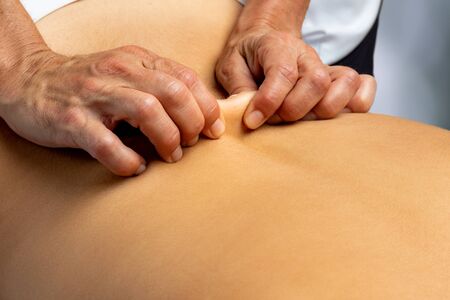 Close up of hands pinching skin on lower back. Therapist grabbing skin next to back spine.の写真素材