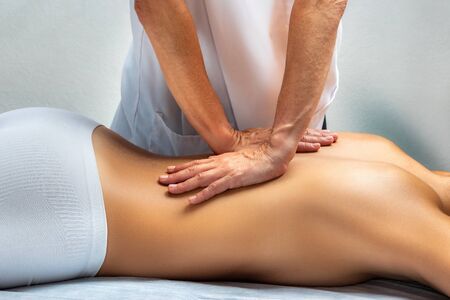 Close up of physiotherapist applying pressure with hands on female back. Young woman lying on spa bed facing down.の写真素材