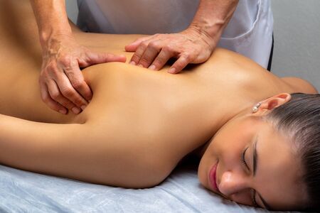 Close up of physiotherapist manipulating shoulder blade on young woman. Girl laying on spa bed with hands massaging shoulder.の写真素材