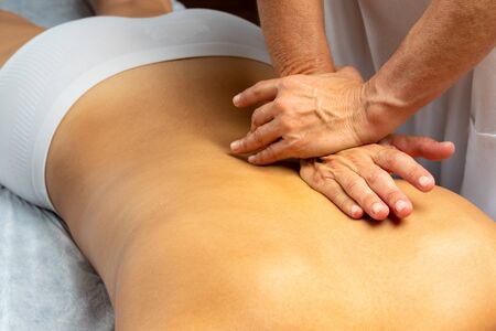 Close up of hands applying pressure along spine on female patient. Woman lying on spa bed with...