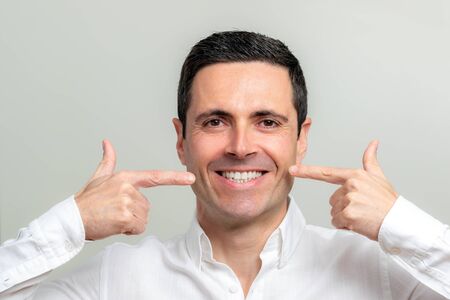 Close up studio portrait of attractive smiling middle aged man pointing with fingers at wrinkles...