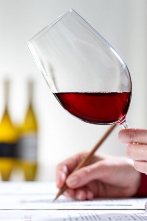 Close up vertical shot of enologist evaluating red wine body and color at table.の写真素材