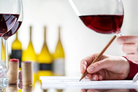 Close up detail of enologist writing notes on wine evaluation at table. Out of focus bottles in background.の写真素材