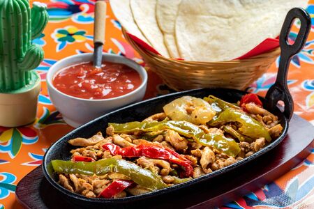 Close up Mexican fajita dish. Spicy grilled chicken with red and green bell peppers and hot tomato sauce. Corn tortillas in background.の写真素材