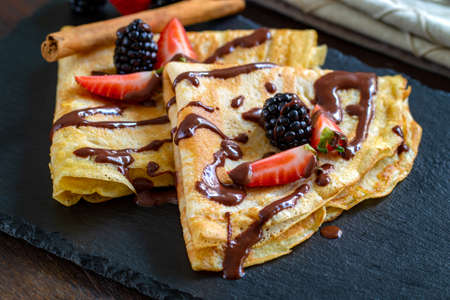 Close up of appetizing thin pancakes with melting chocolate sauce and red fruit dressing.