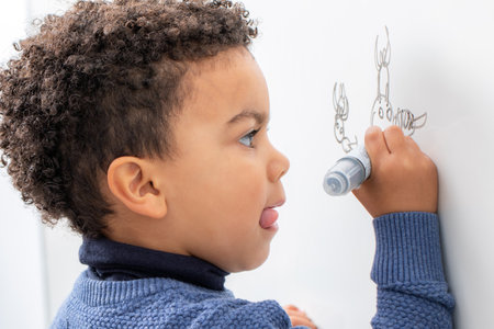 Close up portrait of little afro american boy drawing with marker pen on white board.の写真素材