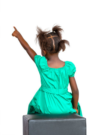 Rear view of little African girl in green dress pointing with finger. Isolated on white background.の写真素材