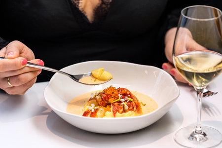 Close up detail of woman having dinner in gourmet restaurant. Female hands holding spoon with lobster soup next to a glass of white wine.の写真素材