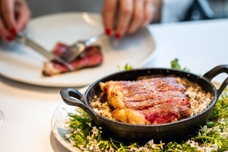 Close up of medium rare  wagyu sirloin steak in iron bowl with woman eating in background.の写真素材