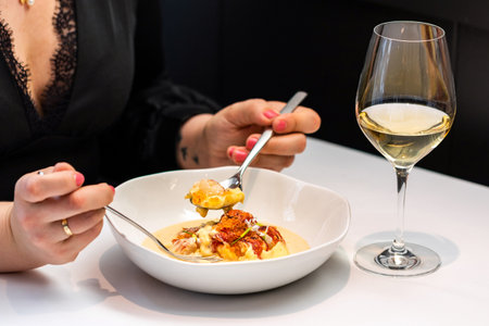 Close up detail of woman having dinner in gourmet restaurant. Female hands holding spoon with lobster soup next to a glass of white wine.の写真素材