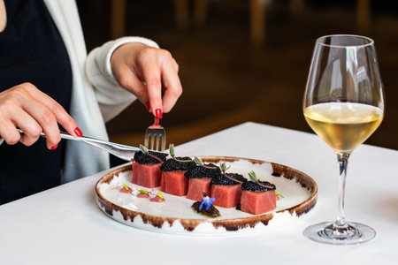 Close up detail of woman having dinner in gourmet restaurant. Macro close up of female hands next to bluefin tuna dish with beluga caviar and a glass of white wine.の写真素材
