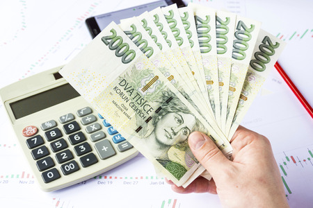Calculator with czech money on economic charts. Mobile telephone on the charts. Stock market trading. Business concept. A hand holding a lot of money over the charts. Drop of money. Work desk economist.の写真素材