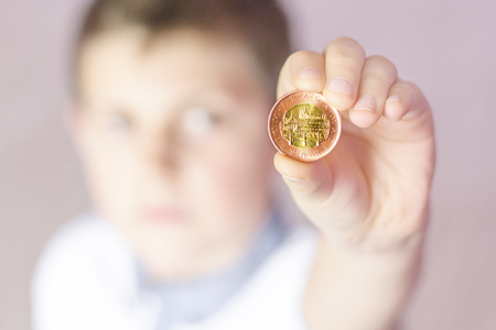 Little boy holding a metal coin in his hand. Boy thinking what to do with savings. Child saving money. Money from the Czech Republic.の写真素材