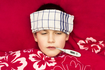 A sick boy lying in bed with a thermometer in his mouthの写真素材