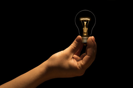 Hand holding a filament lamp on a black background. The bulb as a symbol of an idea. Glowing tungsten bulb. Ecological concept.の写真素材