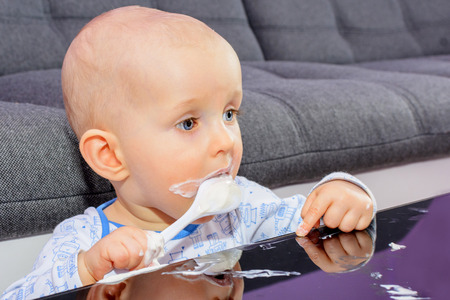 First birthday celebration of a little boy. Little boy eating birthday cake with a spoon, happy birthday. Toddler at table with cake.の写真素材