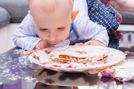 First birthday celebration of a little boy. Little boy eating birthday cake with a spoon, happy birthday. Toddler at table with cake. Little baby smash birthday cake. の写真素材