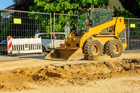 Orange dredger at a building site in the city. Construction of sewerage in the area. Parked work machines on the road. Bulldozer on site. Dropped road.の写真素材