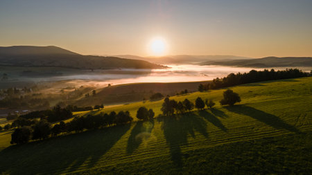 Sunrise in Czech mountains with foggy valley with village and meadows.の写真素材