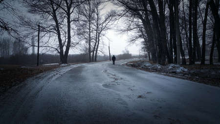 Silhouette of a man walking in the distance on a forest road in winter. There is a lot of snow. A lonely boy walks along a path in a stressful state. Places for text.の写真素材