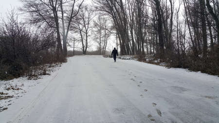 Silhouette of a man walking in the distance on a forest road in winter. There is a lot of snow. A lonely boy walks along a path in a stressful state. Places for text.の写真素材