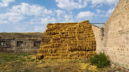 Haystack next to the barn. Stacked straw bales of hay. Square haystack under the open sky. Animal feed. Agricultural background. Concept of the village.の写真素材