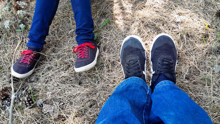 Feet of young lovers sitting next to sports shoes and jeans. The theme of love. Love relationship the boy and girl. Body parts of people on the background of forest soil.の写真素材