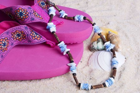sandals and blue necklace on sand at the beach