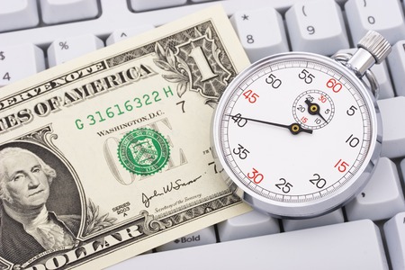 A stopwatch with dollar bill on a white keyboardの写真素材