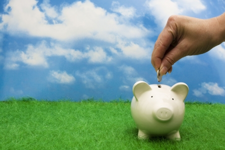 Coin bank sitting on grass with hand putting in a coin Coin bank sitting on grass with hand putting in a coin