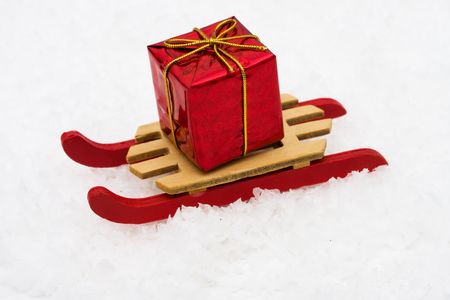 Wooden sleigh sitting on snow with red Christmas present, winter funの写真素材