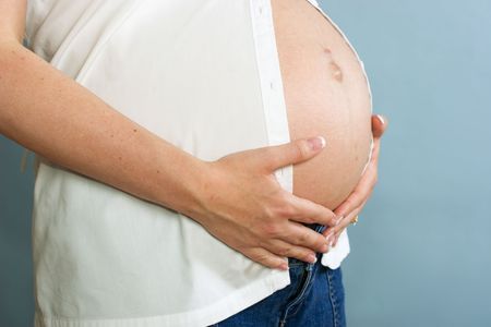 Pregnant woman standing showing her belly on blue background, pregnancy